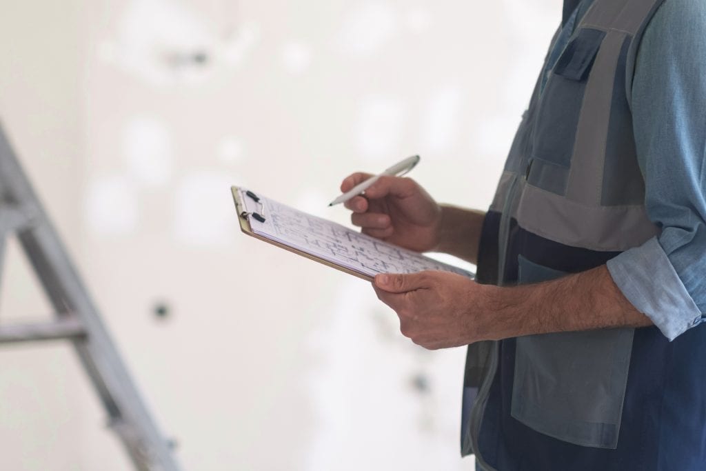 Handwerker mit Klemmbrett überprüft die Wandoberfläche auf einer Baustelle – Symbol für sorgfältige Arbeitsvorbereitung und Qualitätskontrolle bei Pejic Bozo Spachtler in Graz.